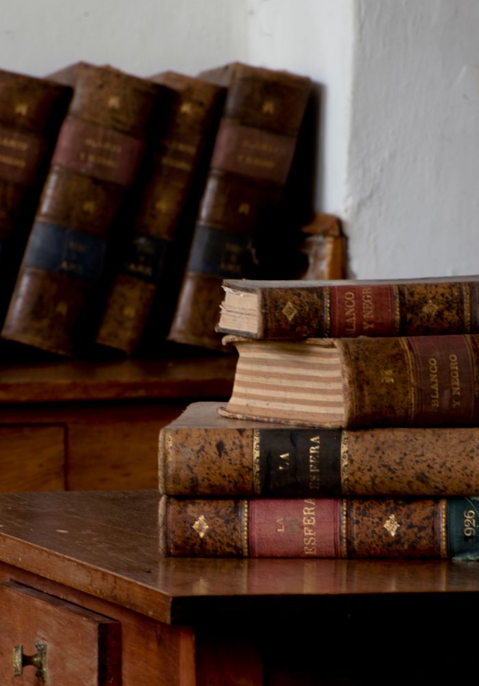 Stack of vintage leather-bound books on an antique wooden desk indoors.